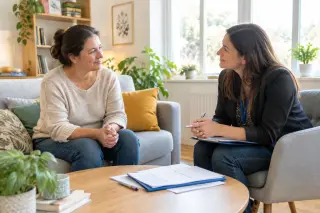 Une femme discute avec une assistante sociale dans un salon lumineux, entourées de documents, ambiance chaleureuse et rassurante.
